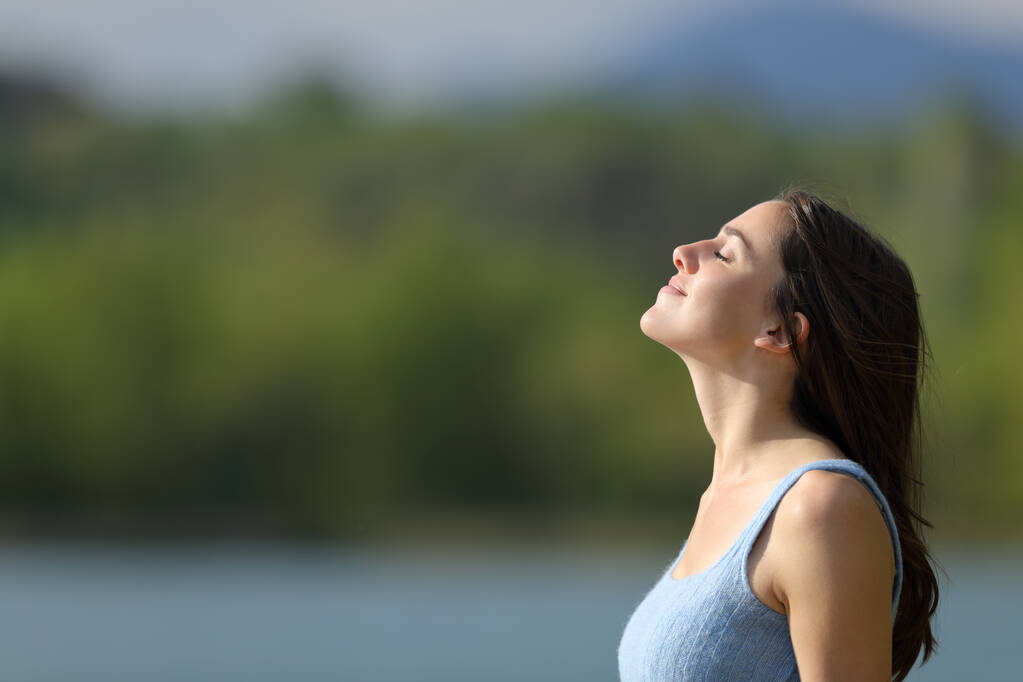Perfil de una mujer relajada respirando aire fresco meditando junto a un lago - Foto, imagen
