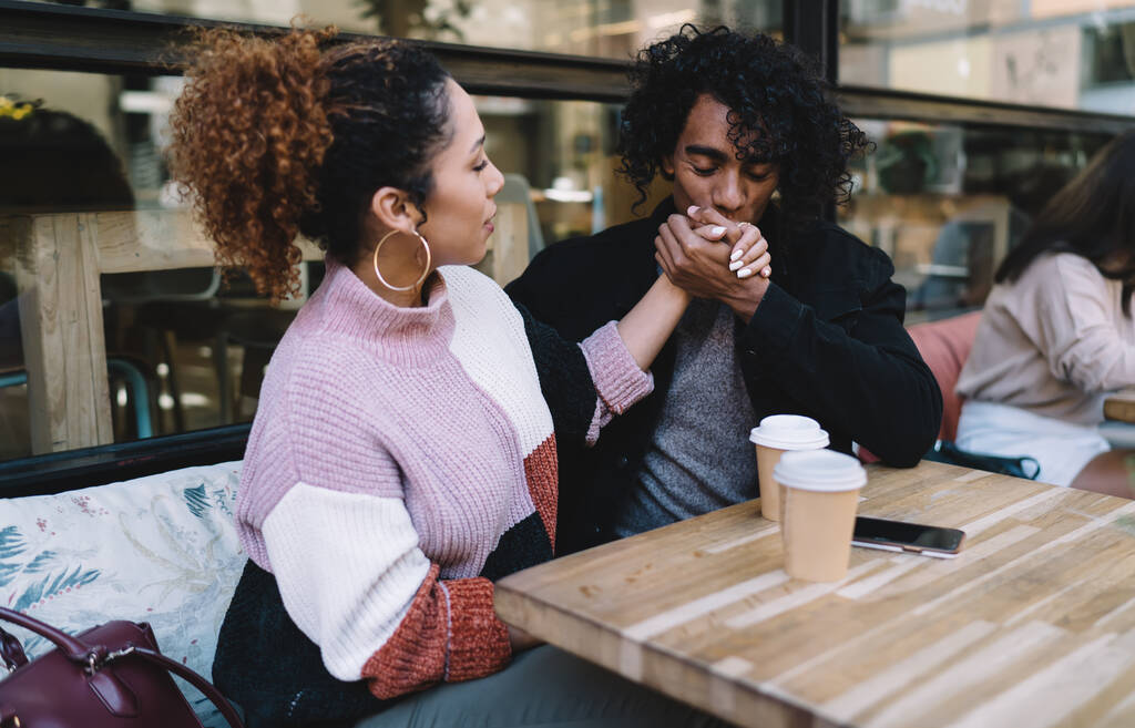 Элегантная молодая женщина с молодым парнем целует подружек рука сидит за столиком с кофе, чтобы пойти в городское кафе - Фото, изображение