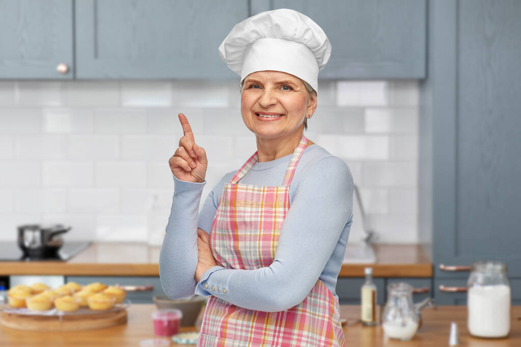 uśmiechnięta starsza kobieta lub szef kuchni wskazujący palcem w górę - Zdjęcie, obraz