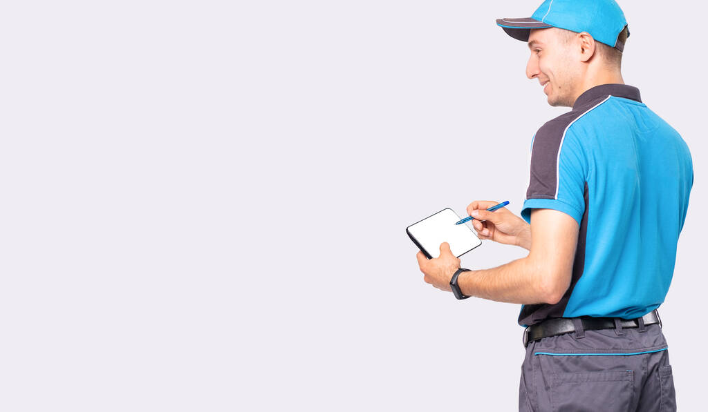 De koerier in blauw uniform maakt bestelling voor de levering van goederen met de pen en de tablet in zijn handen.  - Foto, afbeelding