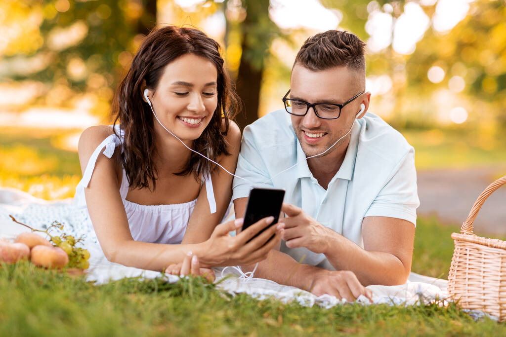 casal com fones de ouvido e smartphone no piquenique - Foto, Imagem