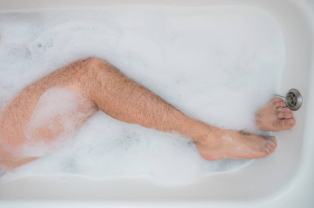 Rahatlatıcı bir banyo yapan bir adamın komik bir fotoğrafı. Köpük banyosunda erkek ayağının yakın çekimi. Üst görünüm - Fotoğraf, Görsel