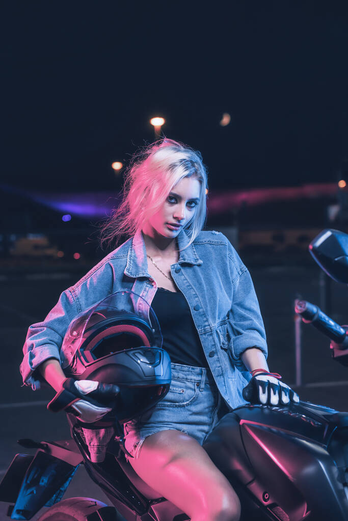 portret dziewczyny w promieniach neonowego światła na motocyklu w nocy na pustym parkingu - Zdjęcie, obraz