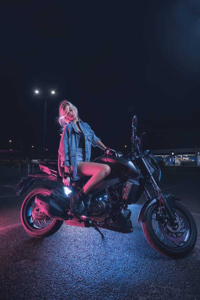 portré egy lányról a neonfényben egy motoron éjszaka egy üres parkolóban - Fotó, kép