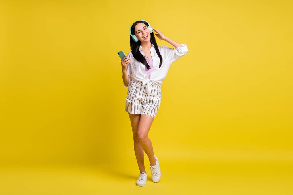 Full size photo of young charming positive girl listen music in headphones using phone isolated on yellow color background - Photo, Image