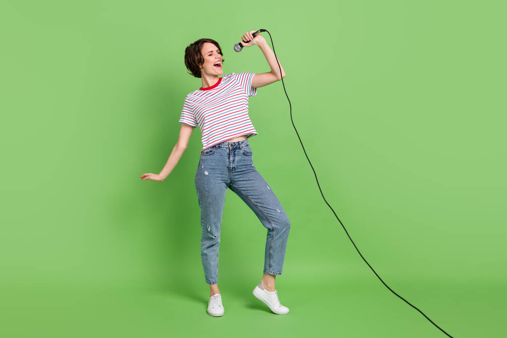 Volledige lichaamsomvang uitzicht van mooie dromerige vrolijke meisje zingen melodie vrije tijd geïsoleerd over groene pastel kleur achtergrond - Foto, afbeelding