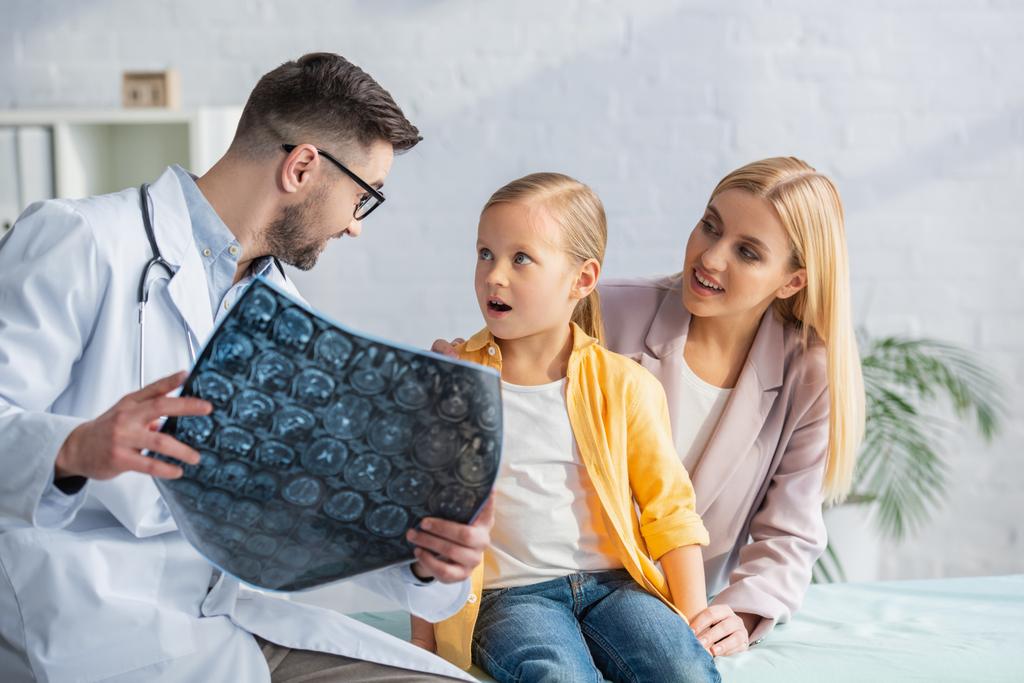 Pediatra che tiene la risonanza magnetica offuscata vicino a bambini e madre stupiti - Foto, immagini