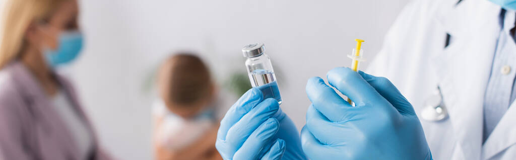 Médecin en gants de latex tenant le vaccin et la seringue près de la mère et de la fille sur fond flou, bannière  - Photo, image