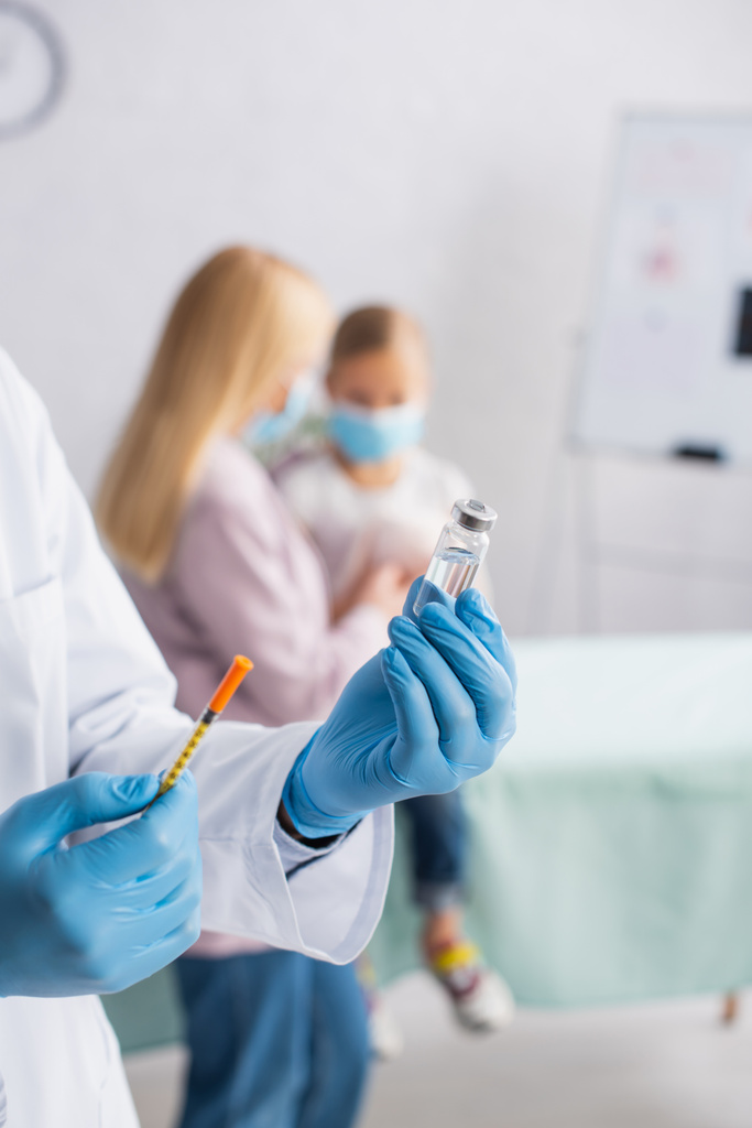 小児科医は、母親と子供の近くにワクチンと注射器を保持  - 写真・画像