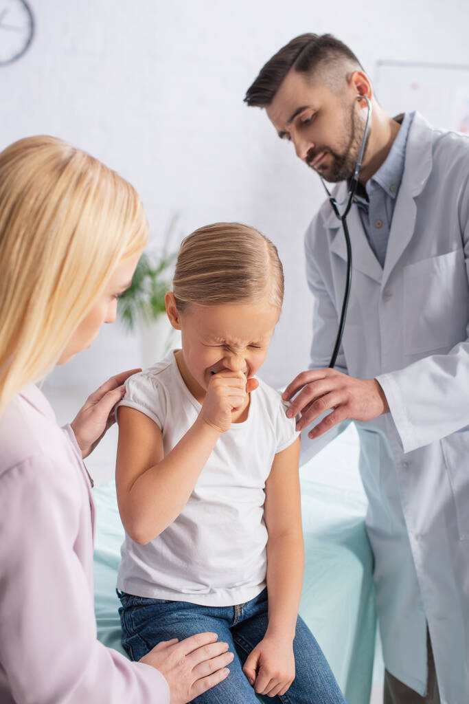 Kind niest in der Nähe von Mutter und Arzt mit Stethoskop  - Foto, Bild