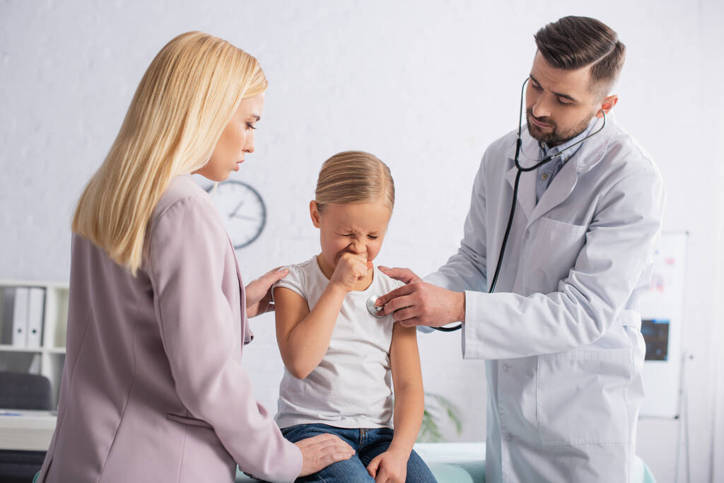 Niño enfermo estornudando cerca de los padres y pediatra con estetoscopio  - Foto, imagen