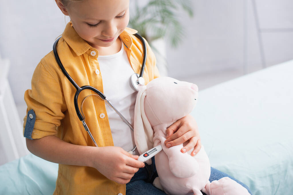 Девушка играет с игрушкой и электронным термометром в больнице  - Фото, изображение