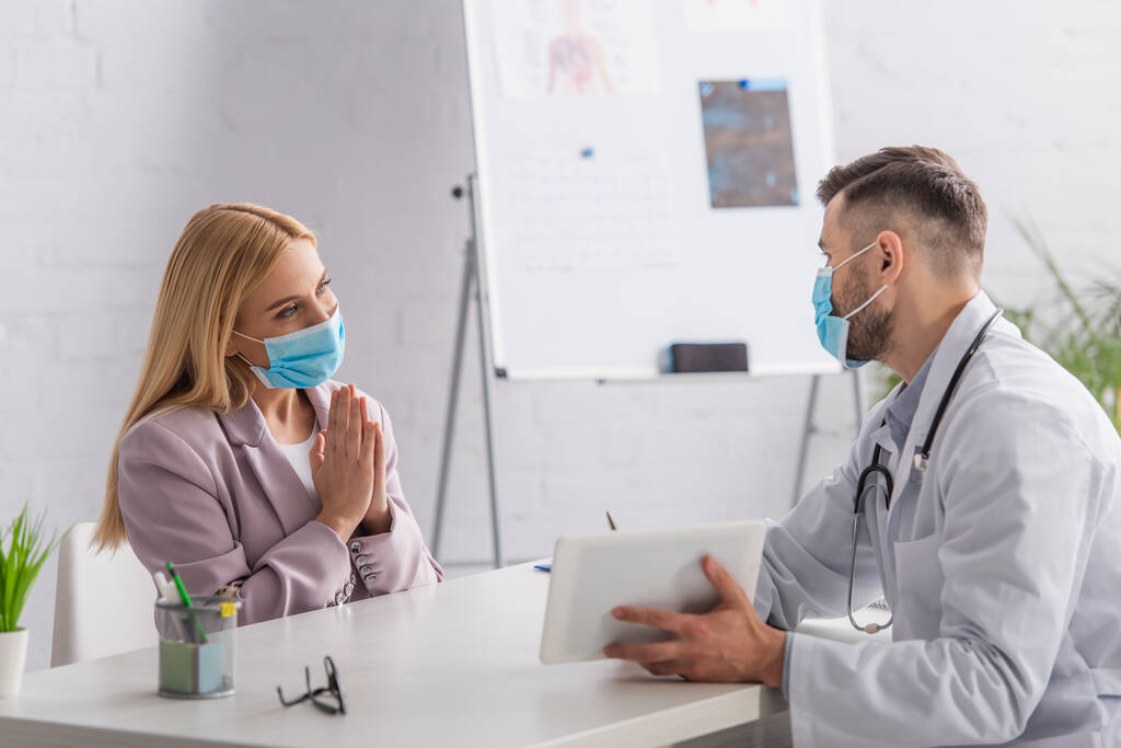 femme en masque de protection montrant s'il vous plaît geste près du médecin avec tablette numérique - Photo, image