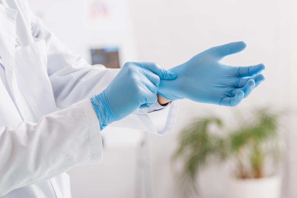 обрезанный вид доктора надевающего голубые латексные перчатки в больнице - Фото, изображение