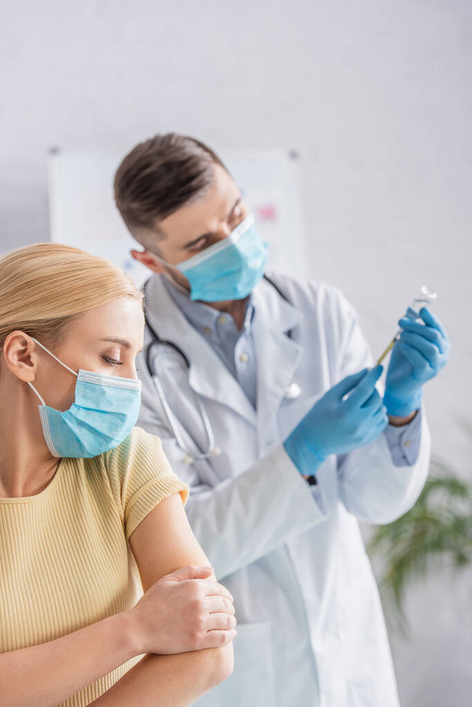 femme en masque médical près d'un médecin remplissant la seringue avec le vaccin - Photo, image