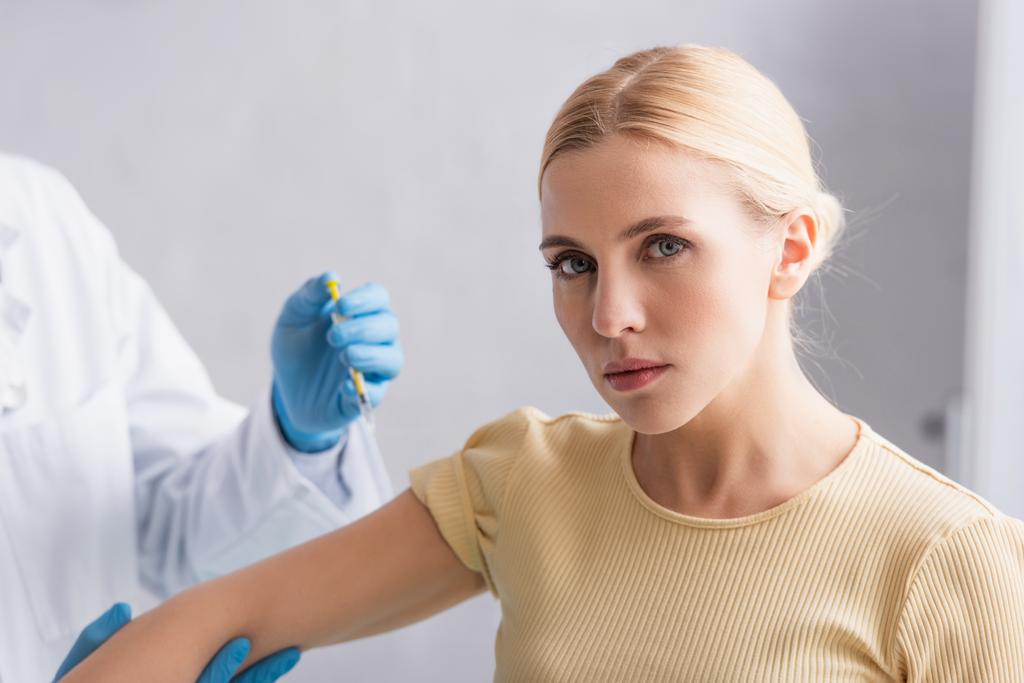 mujer rubia mirando a la cámara durante la vacunación en la clínica - Foto, Imagen