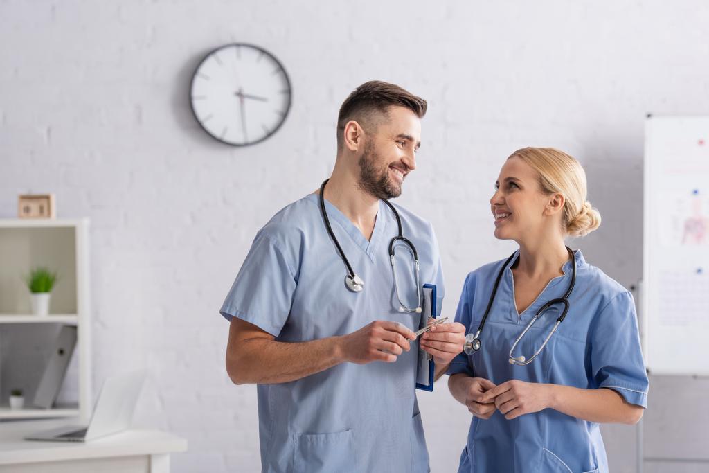 médecins heureux en uniforme bleu se regardant tout en parlant à l'hôpital - Photo, image