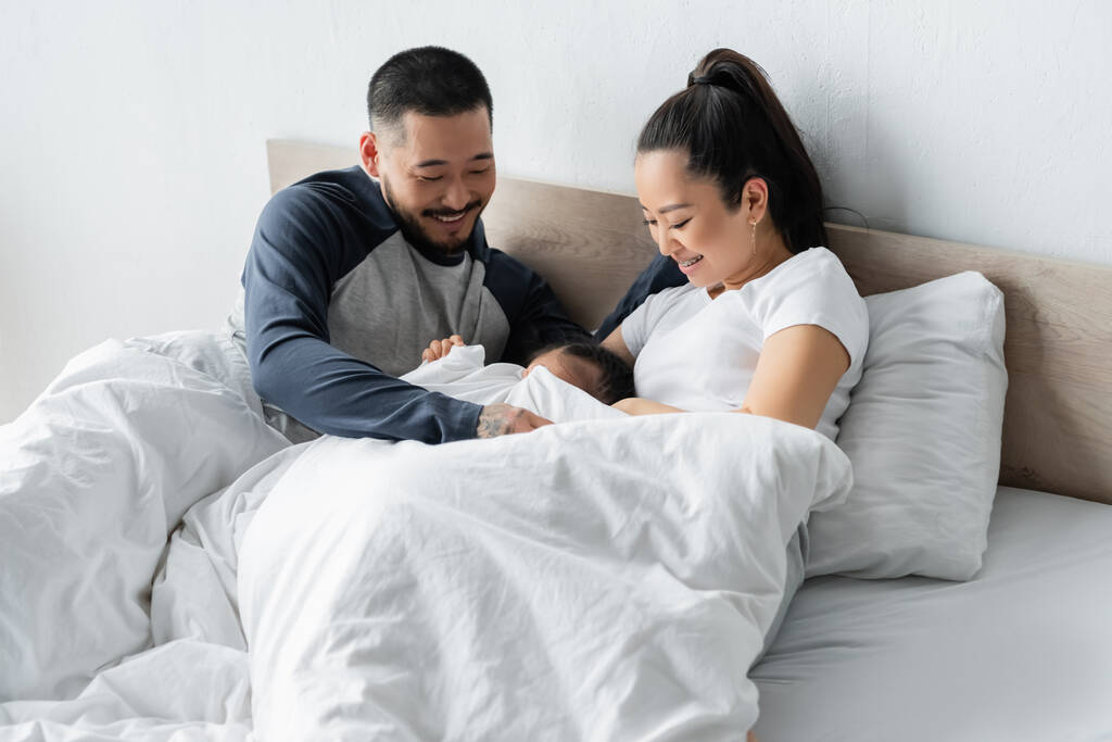 Χαρούμενοι Ασιάτες γονείς κοιτάζουν την κόρη τους στο κρεβάτι - Φωτογραφία, εικόνα
