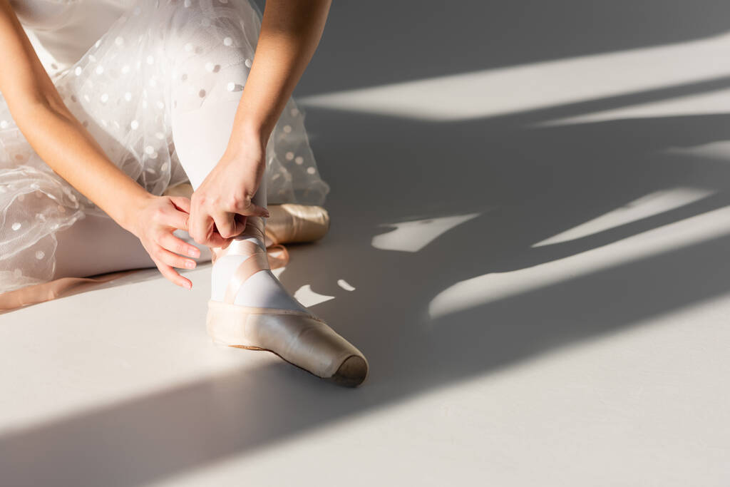 Cropped view of ballerina wearing pointe shoe on grey background with light  - Photo, Image