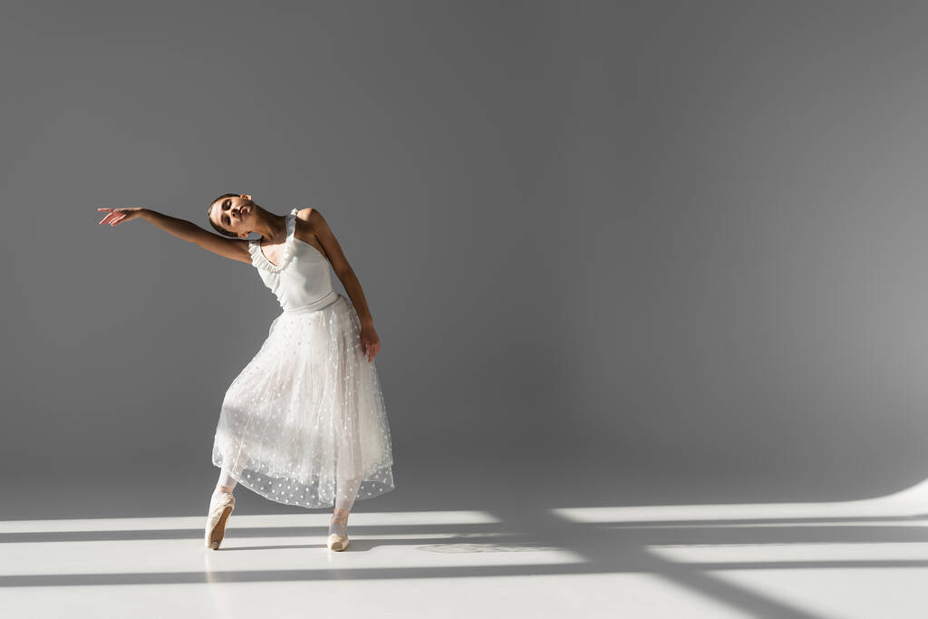 Bailarina bailando con los ojos cerrados sobre fondo gris con luz solar  - Foto, imagen