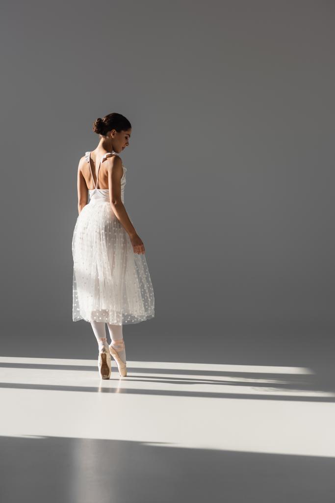 Side view of ballerina in white dress dancing on grey background  - Photo, Image