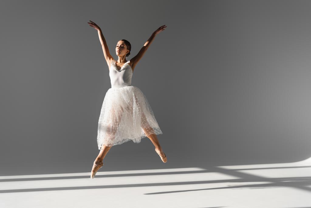 Bailarina joven bailando y saltando sobre fondo gris con luz solar - Foto, Imagen