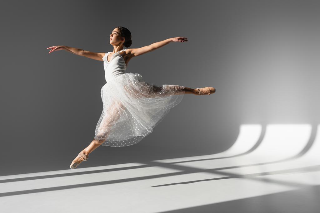 Вид сбоку Фабины в белом платье, прыгающей в солнечном свете на сером фоне  - Фото, изображение