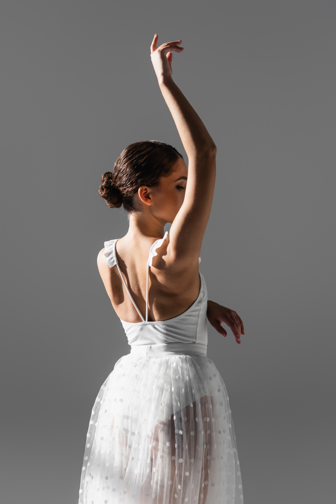 Elegante bailarina levantando la mano aislada en gris  - Foto, imagen