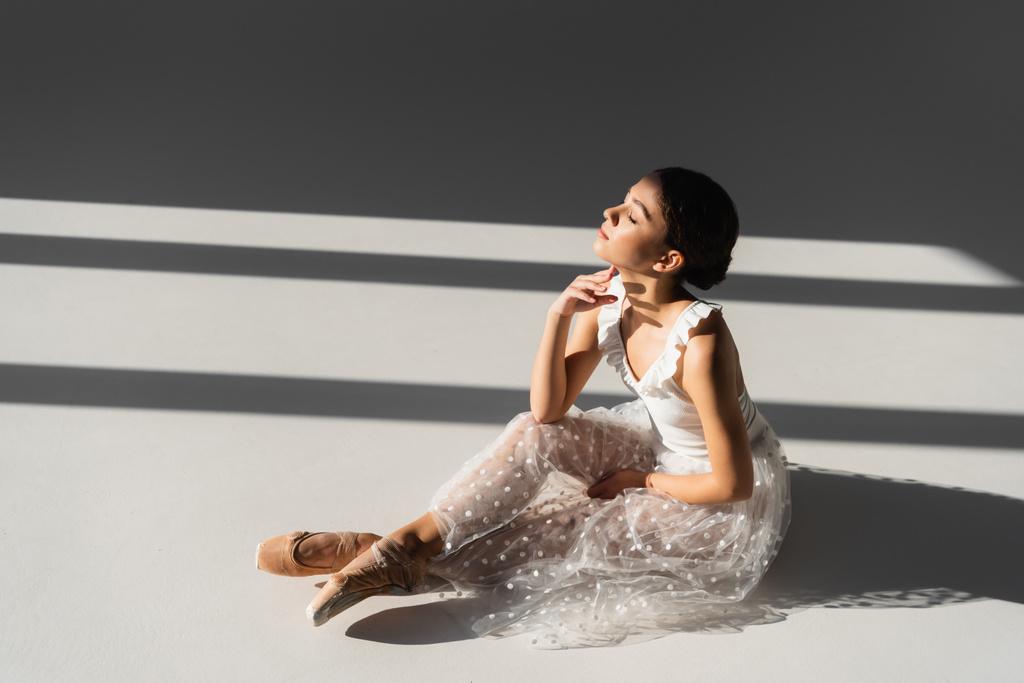 Oldalnézet balerina csukott szemmel ül szürke háttér napfény - Fotó, kép