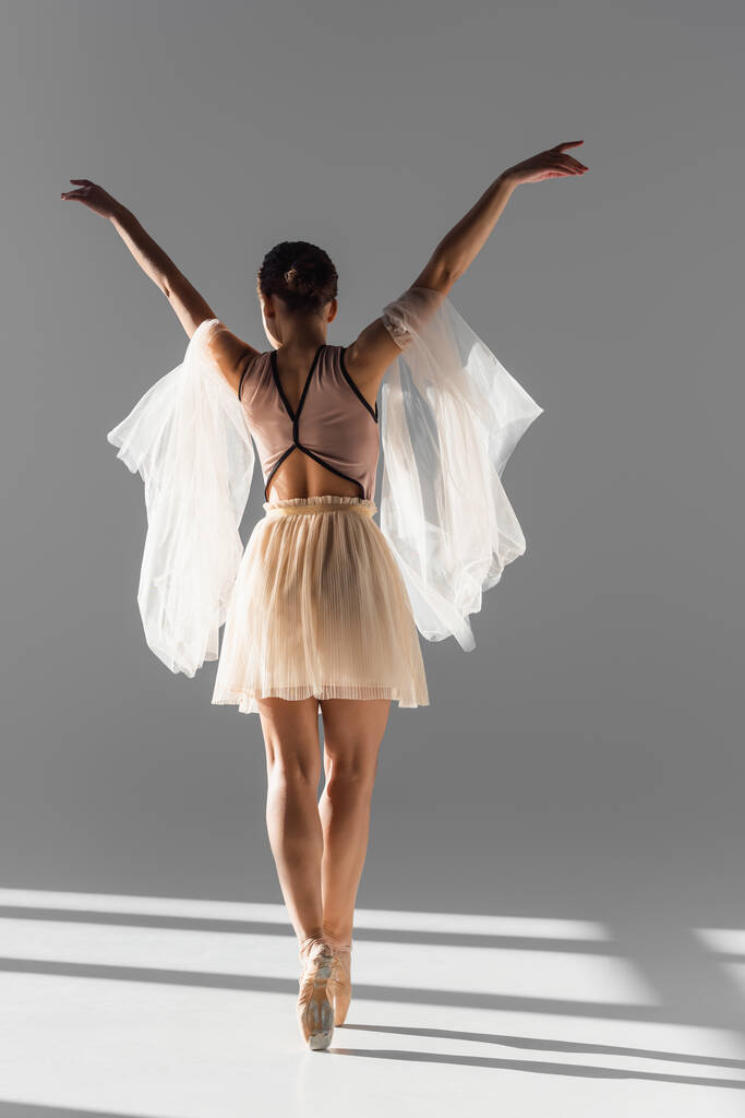Zadní pohled baletky tančící s látkou na šedém pozadí se slunečním světlem - Fotografie, Obrázek