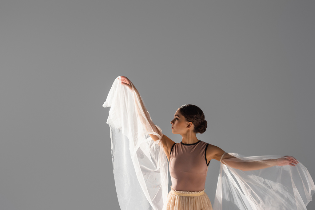 Boční pohled na brunetky balerína tanec s látkou izolované na šedé  - Fotografie, Obrázek