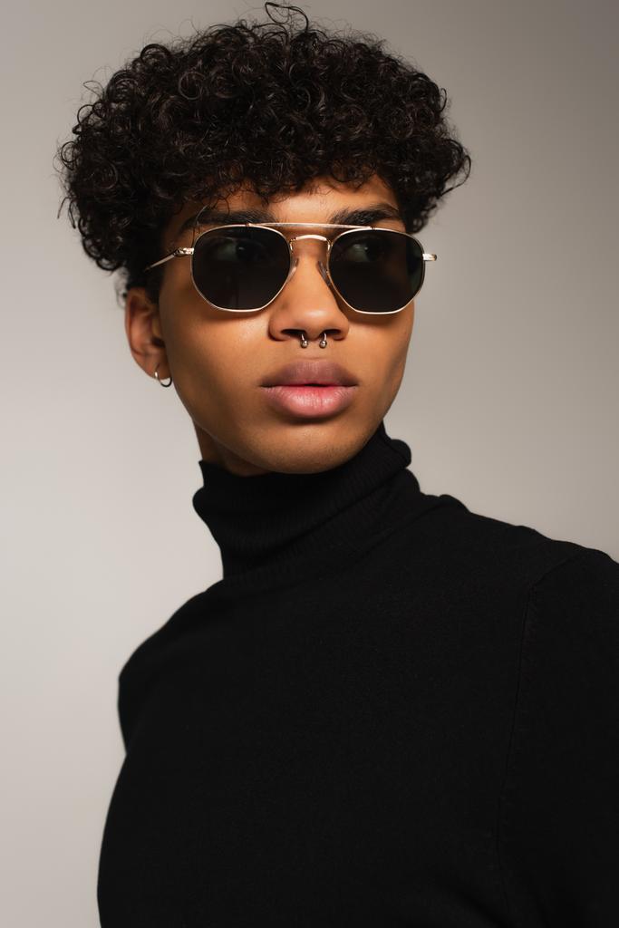 portrait of pierced african american man in dark sunglasses and black turtleneck isolated on grey - Foto, Imagen