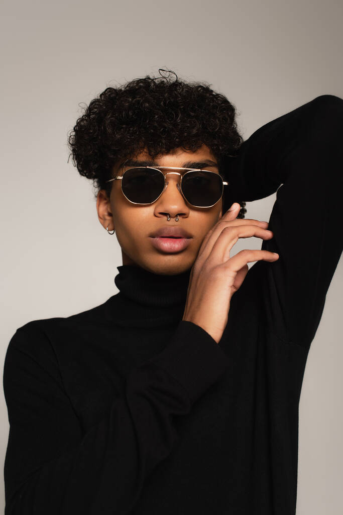 african american man in dark sunglasses and black turtleneck posing with hand behind head isolated on grey - Foto, immagini