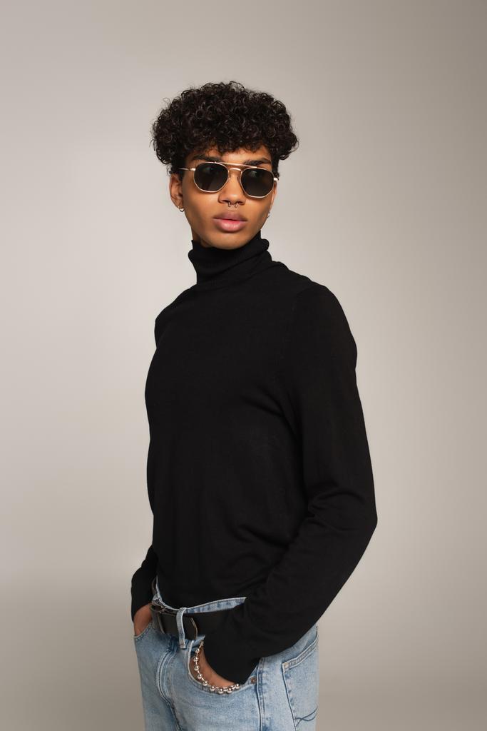 african american man in black turtleneck and sunglasses standing with hands in pockets of jeans isolated on grey - Photo, Image
