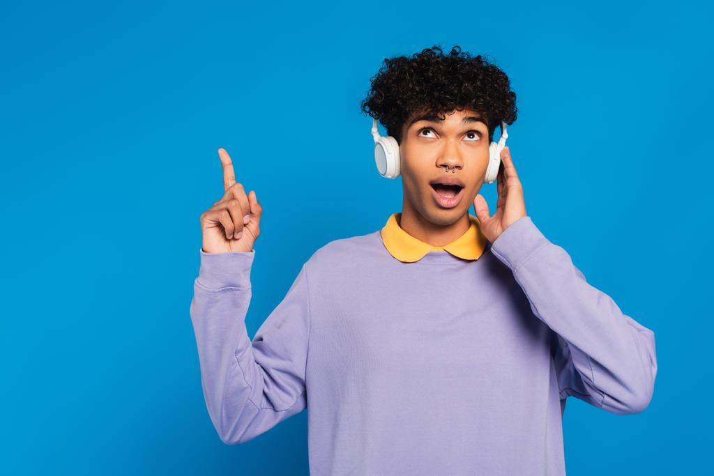 surprised african american man in headphones pointing up with finger isolated on blue - Foto, immagini