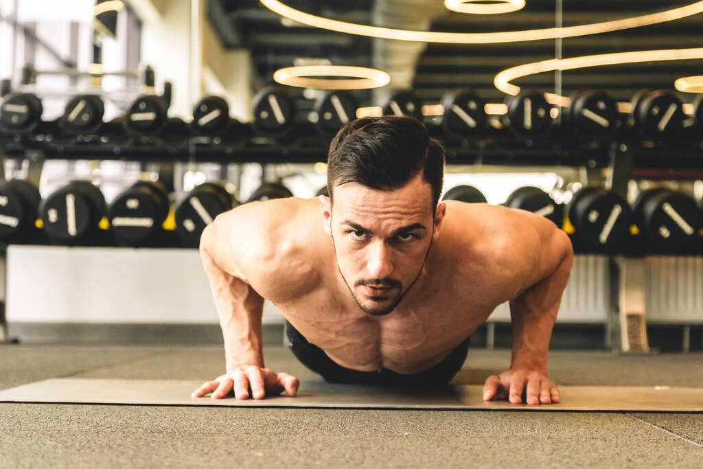 Beau jeune bodybuilder masculin sportif avec torse nu faisant des exercices dans la salle de gym - Photo, image