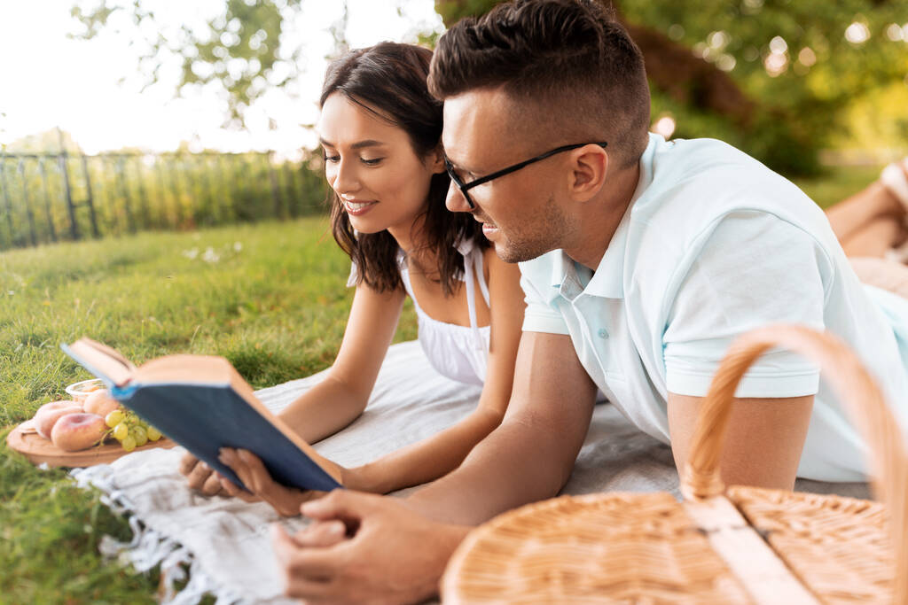 happy couple reading book on picnic at summer park - Photo, Image