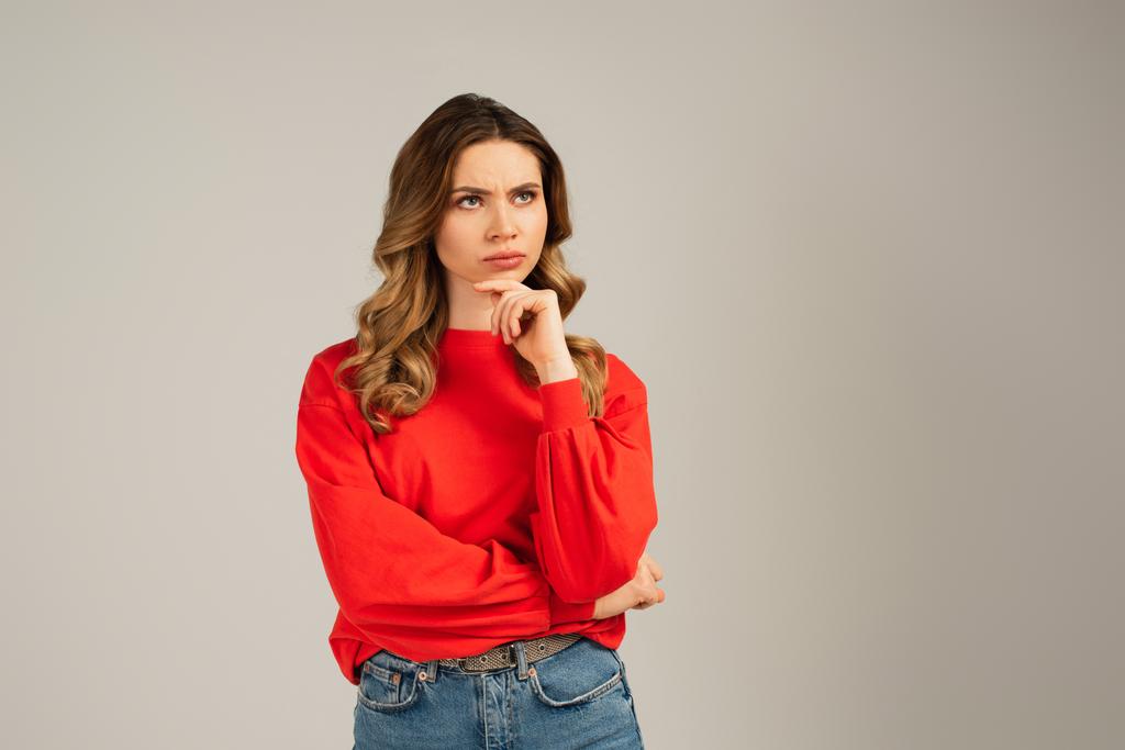 γυναίκα με κόκκινη μπλούζα κοιτάζει αλλού και σκέφτεται απομονωμένη σε γκρι - Φωτογραφία, εικόνα