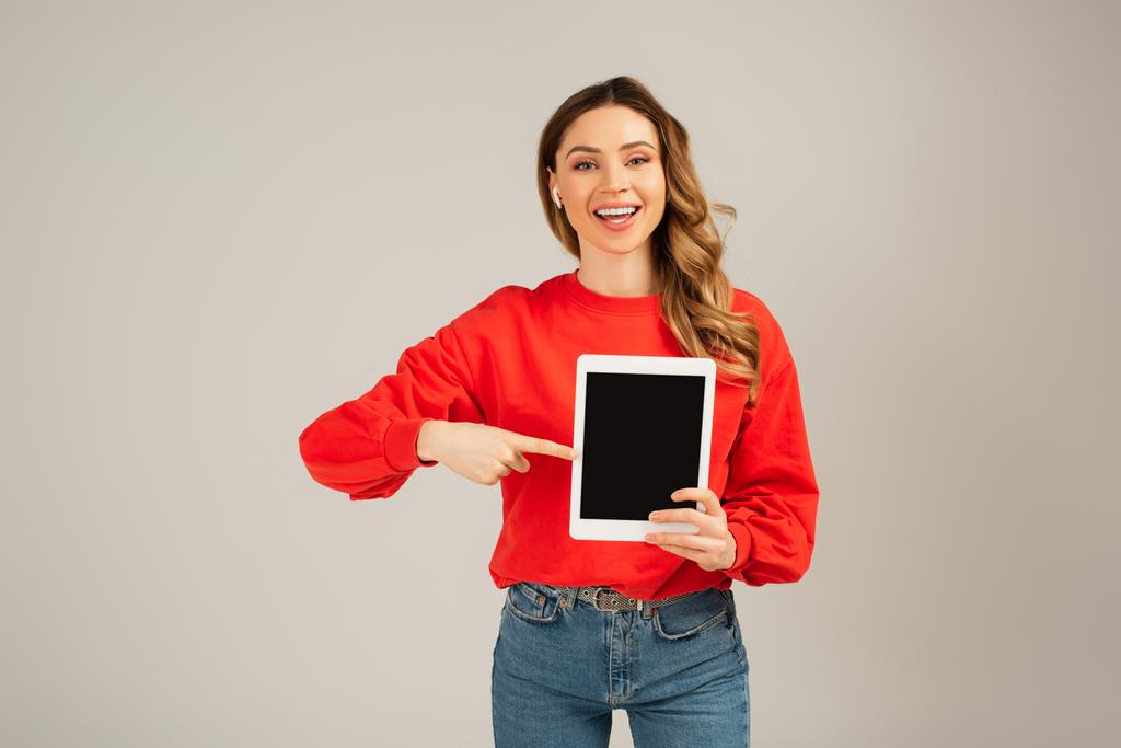 幸せな女性のワイヤレスイヤフォンを指しているデジタルタブレットグレーに隔離された空白の画面で  - 写真・画像