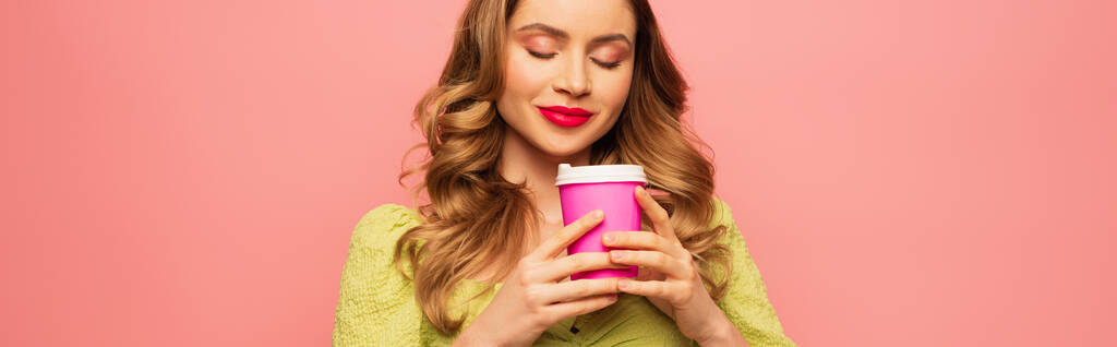 femme heureuse en chemisier vert sentant le café pour aller isolé sur rose, bannière - Photo, image