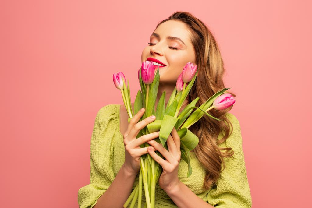 mujer alegre con los ojos cerrados sosteniendo ramo de flores aisladas en rosa - Foto, Imagen