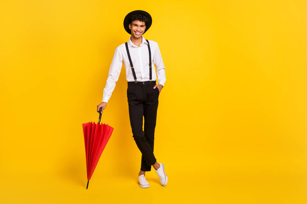 Full length photo portrait of african american guy leaning on red umbrella isolated on vivid yellow colored background - Photo, Image