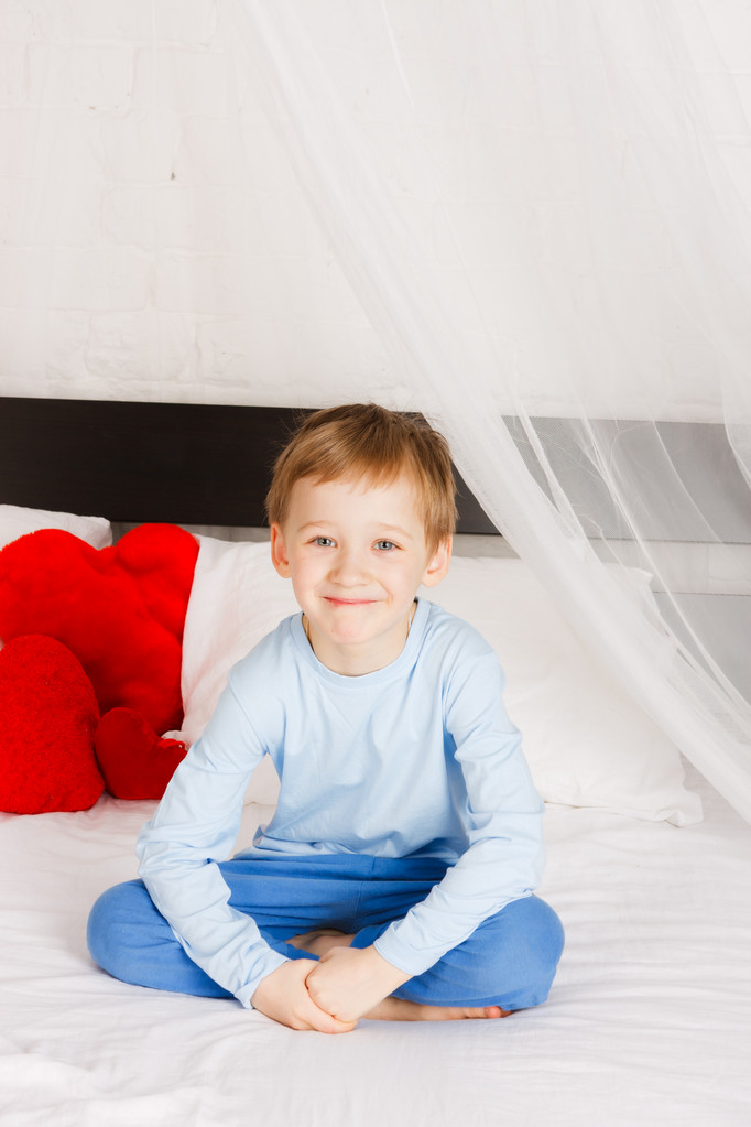 微笑む少年は快適な状況でベッドの上に座っています。 - 写真・画像