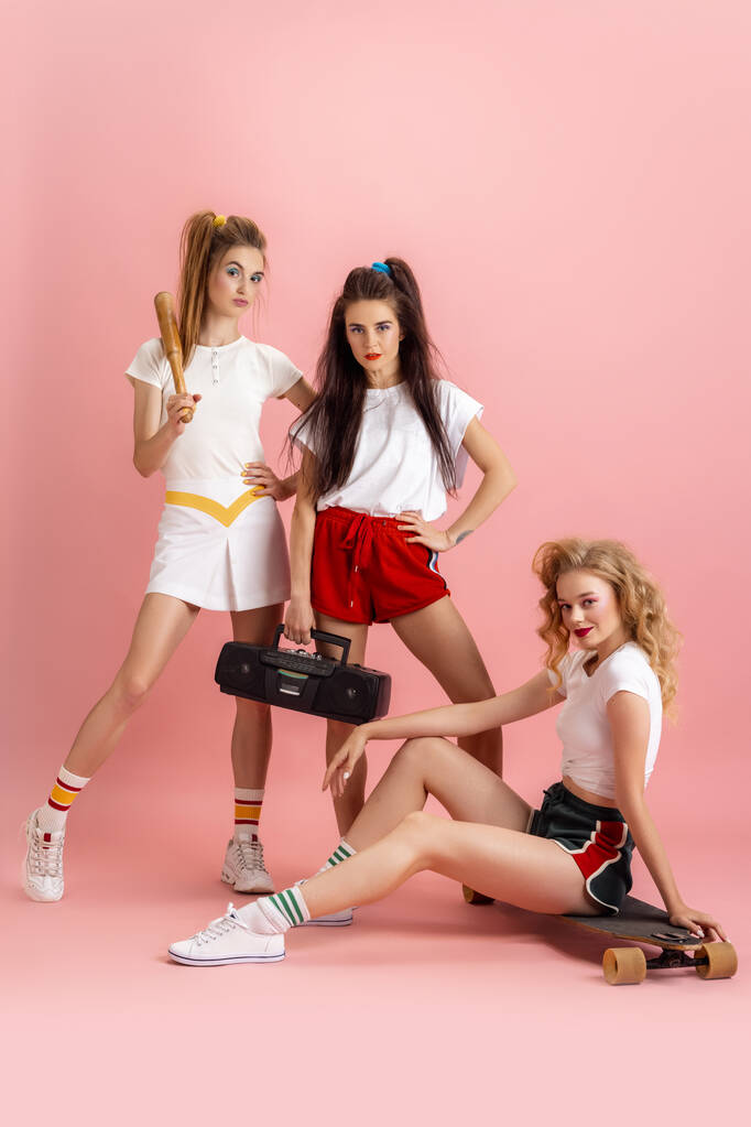 Hübsche junge Frauen im Retro-Stil der 90er Jahre, Outfits, die isoliert vor rosa Studiohintergrund posieren. Konzept des Epochenvergleichs, Schönheit, Mode und Jugend. - Foto, Bild