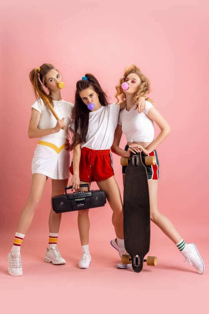 Hübsche junge Frauen im Retro-Stil der 90er Jahre, Outfits, die isoliert vor rosa Studiohintergrund posieren. Konzept des Epochenvergleichs, Schönheit, Mode und Jugend. - Foto, Bild