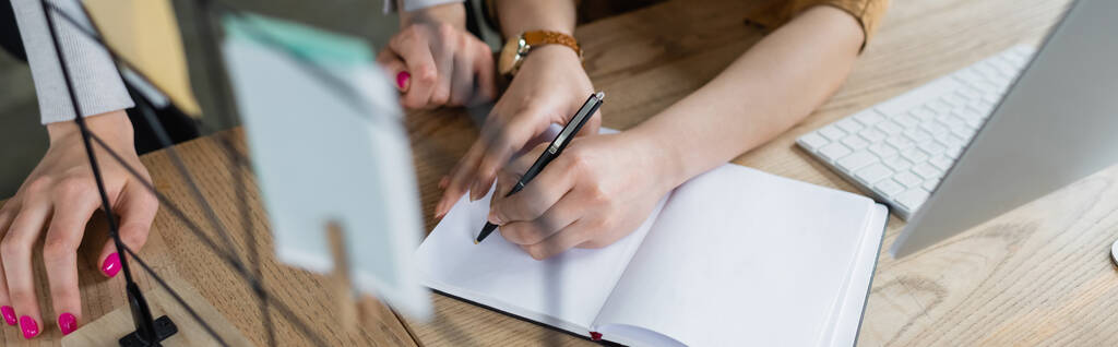 vista recortada de la mujer de negocios escribiendo en cuaderno en blanco cerca de colega, pancarta - Foto, Imagen