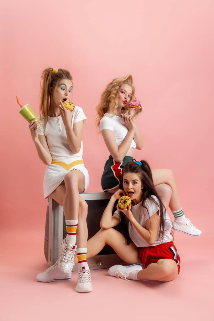 Trzy młode, atrakcyjne kobiety w stylu retro lat 90-tych, stroje pozowane na różowym tle studia. Koncepcja porównywania epok, piękna, mody i młodzieży. - Zdjęcie, obraz
