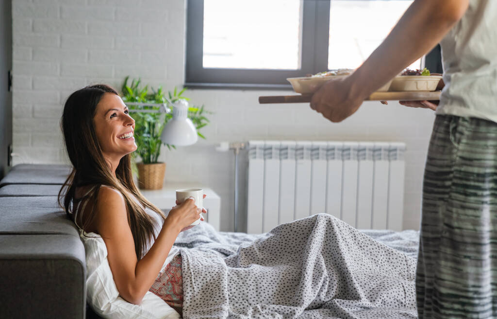 Beautiful young romantic man brings breakfast to woman in the bed and laughing together after wakes up. - Photo, Image