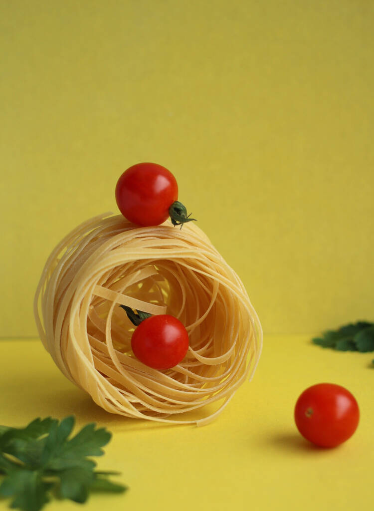 Pasta in the form of a nest with tomatoes and parsley on a yellow background. balance of products - 写真・画像