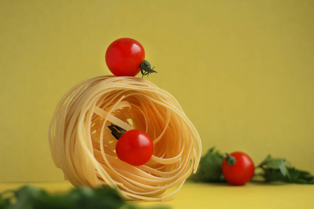 Pasta in Form eines Nestes mit Tomaten und Petersilie auf gelbem Hintergrund. Gleichgewicht der Produkte - Foto, Bild